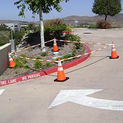 5.5' - 10.5' Orange and White Cone Bars (#150610A-CBOW) with 4x 28" Enviro-Cones cordoning off a section of parking lot landscaping.